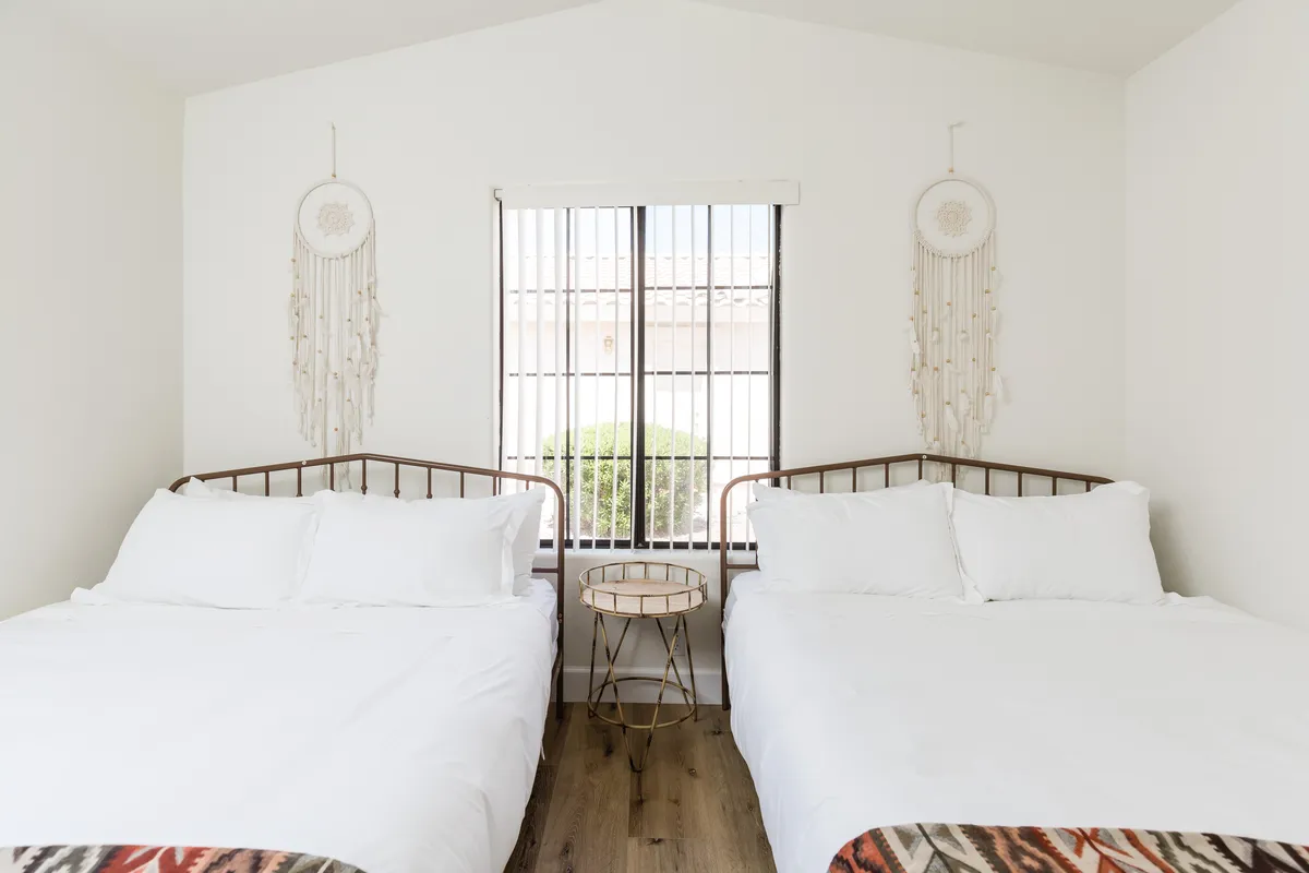 A cozy bedroom with two double beds, dreamcatchers above the beds, a side table, and a window letting in natural light. The arrangement is ideal for groups needing extra sleeping space and fosters a sense of togetherness.