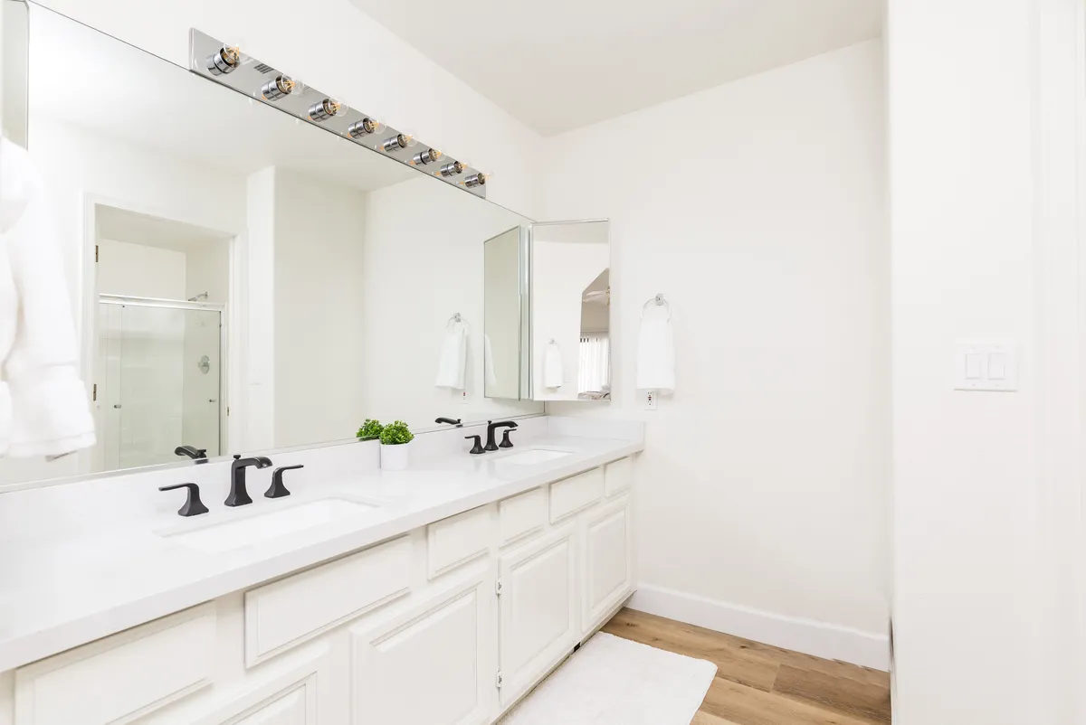 A modern bathroom featuring double sinks, a large mirror, and stylish fixtures, illuminated by natural morning sunlight. The spa-like atmosphere is both practical and relaxing, ideal for self-care routines.
