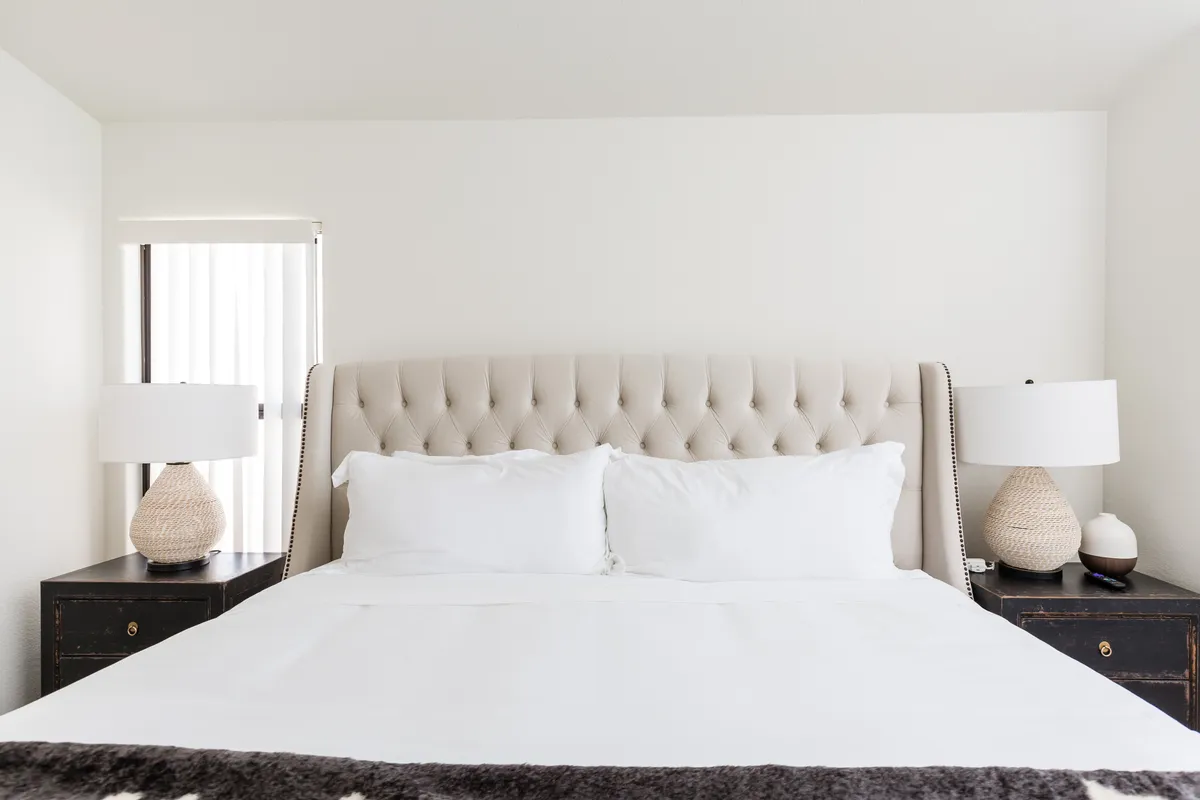 A tranquil bedroom with a tufted headboard, white bedding, and matching decorative lamps on bedside tables. The room exudes a peaceful and inviting atmosphere, perfect for relaxing after a day in the desert.