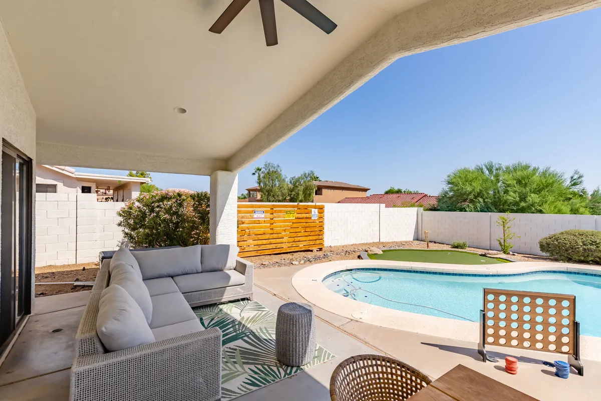 An inviting outdoor pool area with comfortable seating, a decorative wooden privacy wall, and lush landscaping. The setting is perfect for sunbathing or unwinding with a partner, especially during sunset.