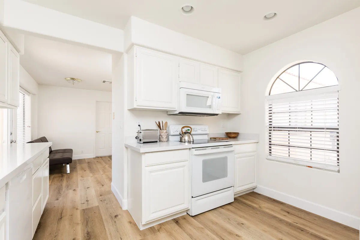 A bright kitchen with white cabinetry, modern appliances, an arched window, and a central island. The space is cheerful and open, perfect for preparing family meals, using the provided kitchen starter kit, or setting up extra baby gear or pet essentials.