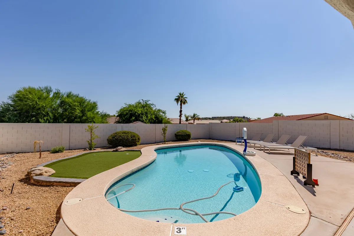 A luxurious backyard pool area featuring lounge chairs, a palm tree, and a neatly manicured grass area. The setting is designed for relaxation, with warm lighting suggesting the perfect place to unwind after a day on the course.