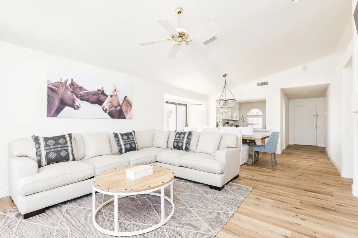 A bright, open living room featuring a large sectional sofa centered around a round coffee table, with modern horse-themed artwork adding a touch of desert-inspired décor. The space feels airy and inviting, perfect for gatherings, relaxation, or entertainment.