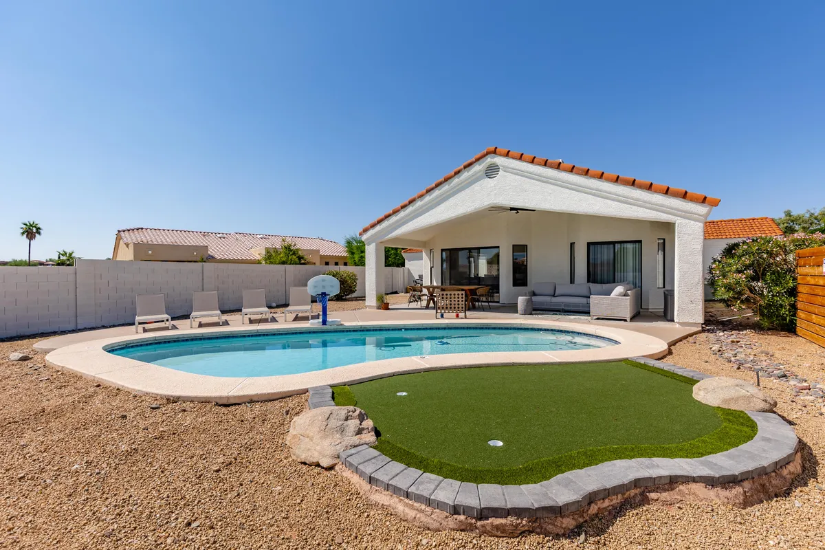 The image showcases a sparkling swimming pool surrounded by sun loungers, an inviting outdoor seating area, and a well-manicured putting green—all set against the scenic backdrop of Fountain Hills, Arizona. The space is perfect for relaxing, entertaining, and enjoying the warm desert sun.